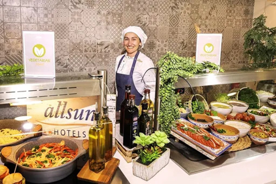 Frau mit Kochm&uuml;tze und Kochsch&uuml;rze steht hinter einem Buffet